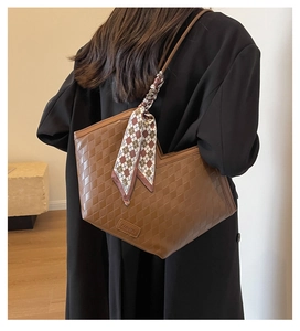 Brown woven tote bag with checkered scarf detail shown on shoulder in a lifestyle setting