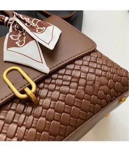 Detail of a brown woven crossbody bag featuring a golden oval buckle and silk scarf accent