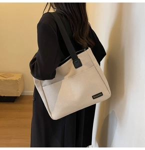 Detail of off-white canvas tote bag featuring black wide strap and branded leather label