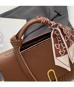 Detailed close-up of brown handbag with woven texture, silk scarf, and gold buckle