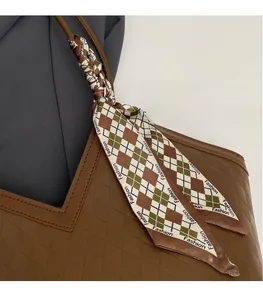 Detail of checkered silk scarf tied on a brown textured tote bag handle with fashion logo