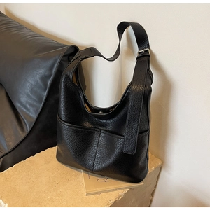 Détail d'un sac seau noir en cuir texturé litchi avec large bandoulière réglable et poches