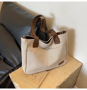 Detail of canvas tote bag with brown straps, large front pocket and leather logo patch