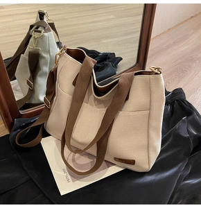 Detail of canvas tote bag with side pocket, brown straps, and leather logo on wood floor