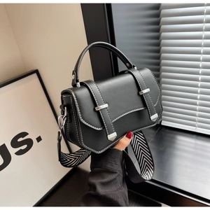 Close-up of black crossbody bag with white contrast stitching and wide woven strap
