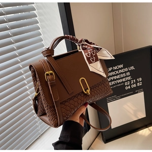 Detail of a brown leather bag with woven texture, gold lock, and teddy bear scarf