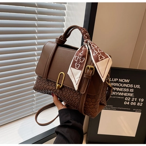 Detail view of dark brown woven textured handbag with golden lock and silk scarf decor