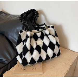 Detail of checkered plush tote bag featuring black chain handle and branded logo patch