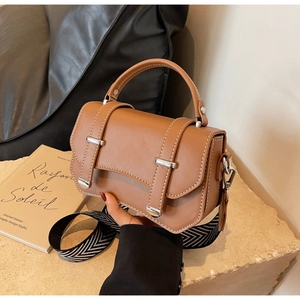 Detail of caramel brown satchel featuring silver buckles and herringbone woven strap