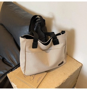 Detail of canvas tote bag with black handles and reinforced leather stitching on stone base