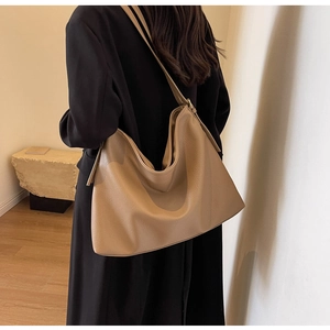 Detailed view of khaki pebbled leather tote bag with wide shoulder strap worn by model