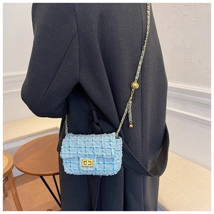 Detail view of light blue tweed shoulder bag with gold chain strap and metal ball buckle