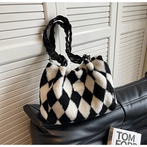 Detailed close-up of plush checkerboard tote bag with braided handles on black leather sofa