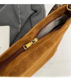 Detail of smooth gold metal zipper and ethnic woven strap on brown suede tote bag