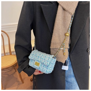 Detail of light blue tweed crossbody bag with gold chain strap and metal ball decoration