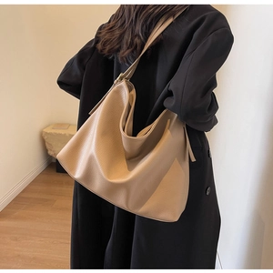 Detail of khaki leather tote bag with lychee texture carried by a model in black coat