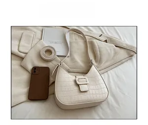 Detail view of cream white croc-embossed underarm bag with elegant crescent shape