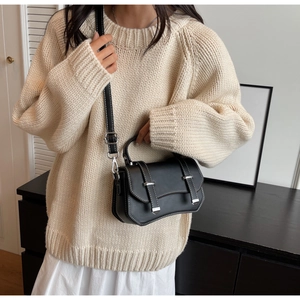 Detail of black crossbody bag with white contrast stitching and silver metal buckles