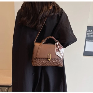 Close-up of brown textured weave bag with metal ring lock and silk scarf handle detail