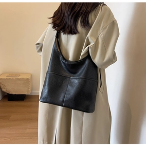 Gros plan du sac cabas noir en cuir grainé porté à l'épaule sur un trench-coat