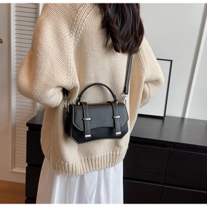 Detail of black crossbody bag with white contrast stitching and silver buckles on a model
