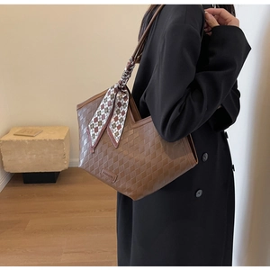 Close-up of brown tote bag featuring diamond quilted texture and a checkered scarf