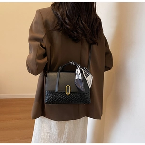 Detail of black crossbody bag with woven texture, golden buckle and printed silk scarf