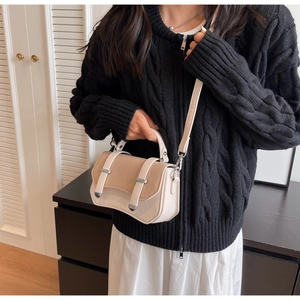 Side view of model holding a beige and white two-tone satchel with metal buckle details