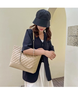 Détail du grand sac cabas matelassé beige avec bandoulière en chaîne porté par un modèle