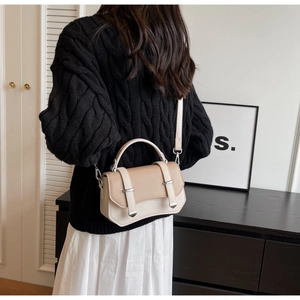 Detail of a two-tone crossbody bag with silver buckles and a structured handle