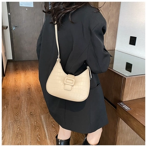 Detail of beige hobo bag with crocodile embossing worn by a model in a blazer