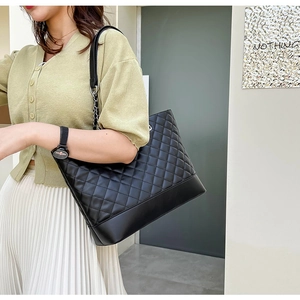 Detail view of large quilted tote bag with metal chain strap on model for daily commute