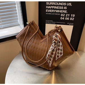 Detail of a brown woven tote bag with a V-shaped top and decorative fashion scarf
