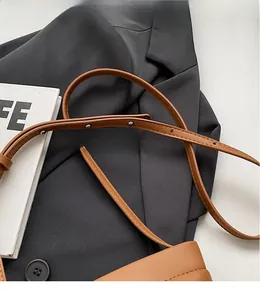 Détail d'une bandoulière en cuir marron réglable avec coutures fines sur un blazer gris