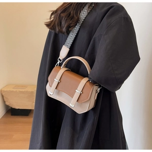 Detail of two-tone crossbody bag with herringbone wide strap worn on black coat