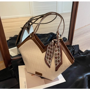 Detail of a contrast quilted tote bag with brown leather handles and a silk scarf wrap