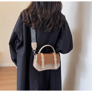 Detail of a brown and beige leather crossbody bag with a wide geometric wave shoulder strap
