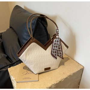 Detail of quilted tote bag with V-cut edge, brown handles, and plaid scarf ornament