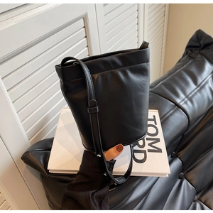 Détail du sac seau en cuir noir minimaliste tenu par un mannequin dans un décor moderne