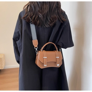 Close-up of brown leather crossbody bag with patterned wide strap worn by a model