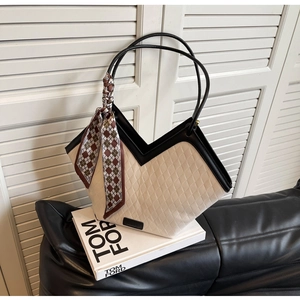 Detail of a geometric V-shaped tote bag with quilted texture and silk scarf handle