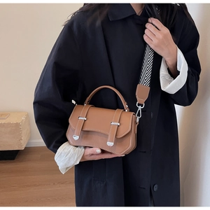 Detail of a brown leather crossbody bag with a wide geometric strap on a black coat