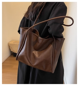 Detail view of large dark brown leather tote bag worn by model in a minimalist setting