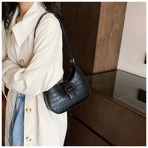 Detail of black faux crocodile embossed hobo bag worn with a beige coat