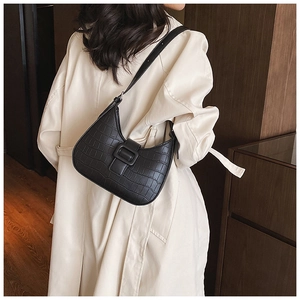 Detail of black croc-effect hobo bag with square buckle worn with a beige trench coat