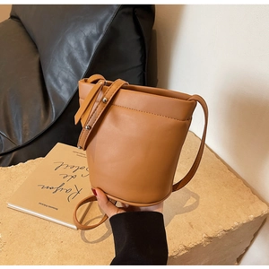 Gros plan d'un sac seau en cuir marron minimaliste sur une surface texturée neutre