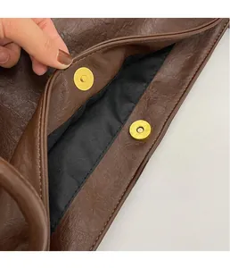 Detail of brown leather tote showing dual gold magnetic clasps and textured grain