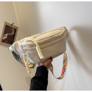 Close-up of cream canvas belt bag with floral jacquard strap and woven zipper pulls