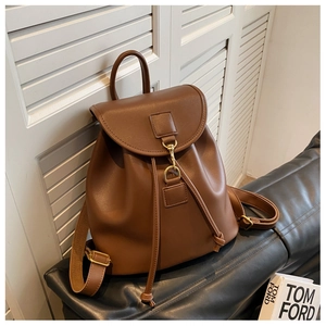 Détail d'un sac à dos en cuir marron montrant le crochet doré et le cordon de serrage