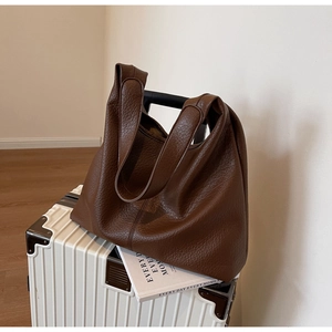 Close-up of brown litchi pattern leather tote bag with wide strap on a white suitcase